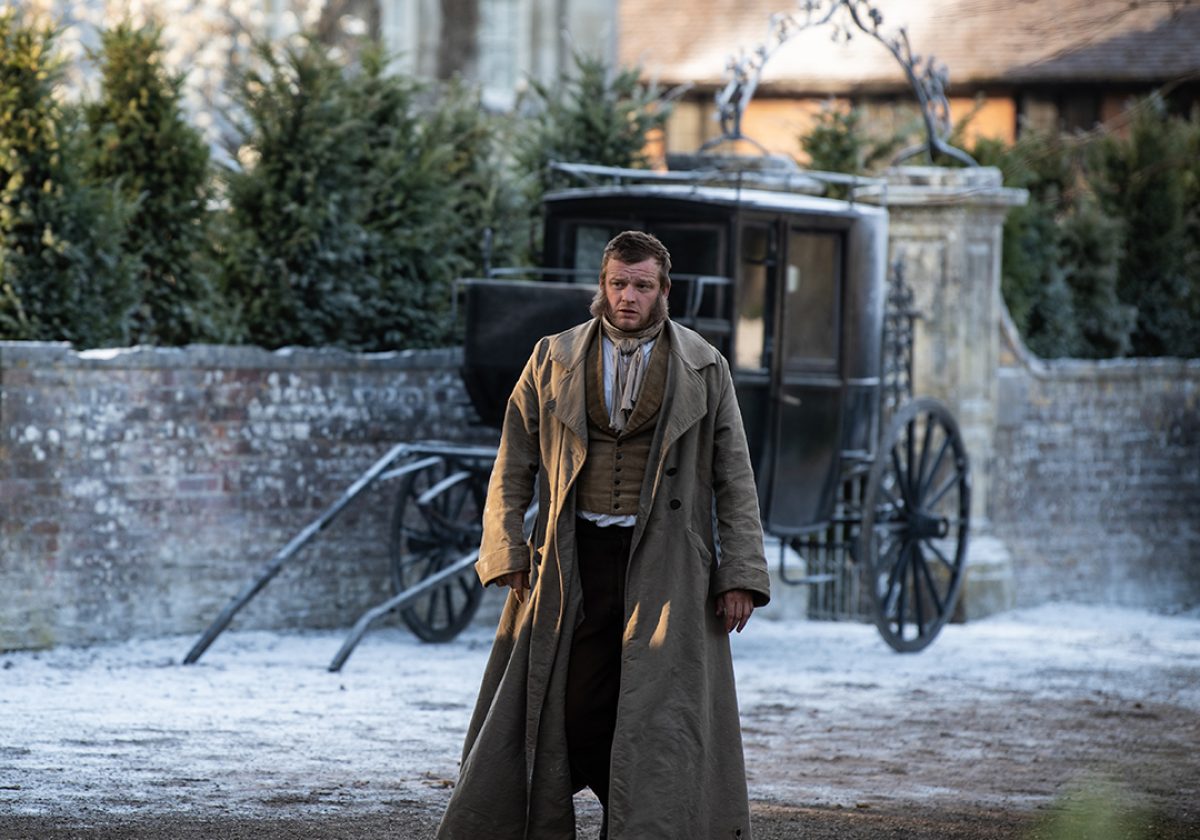 Man in 19th century costume in front of a passenger cart