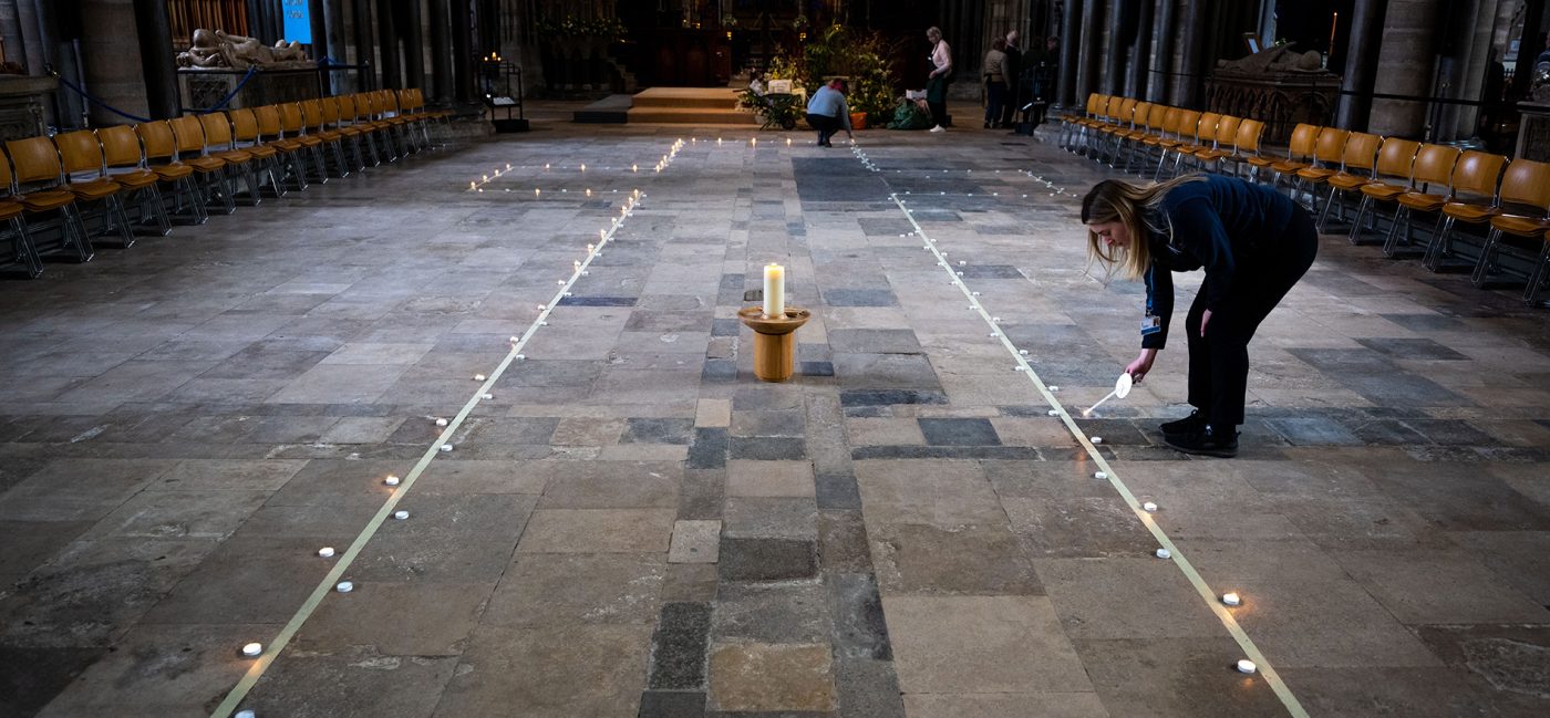 A line of candles marking out a cross on the floor. A woman is lighting a candle on the edge.