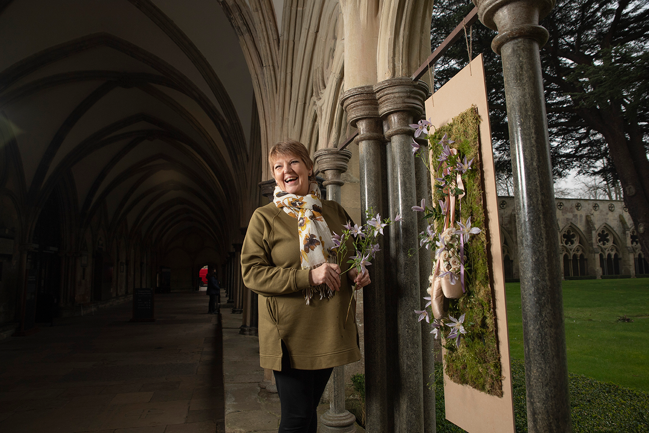 Woman holding flowers, smiling and looking to the side. She's in front of a flower sculpture.