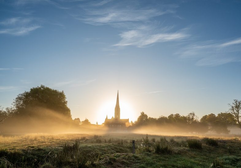 The Cathedral seen at sunrise from across the watermeadows in the West, with the light haloed behind the building.
